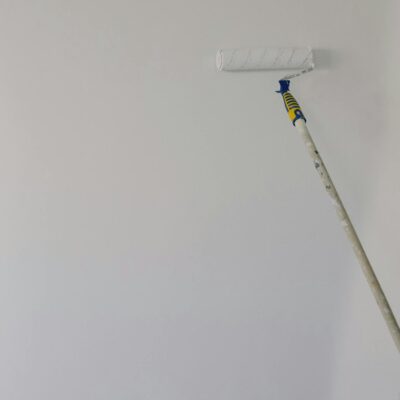 Paint roller with white acrylic paint on wall in room during renovation at home