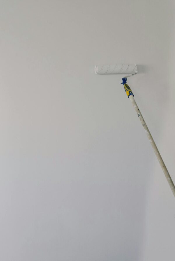 Paint roller with white acrylic paint on wall in room during renovation at home